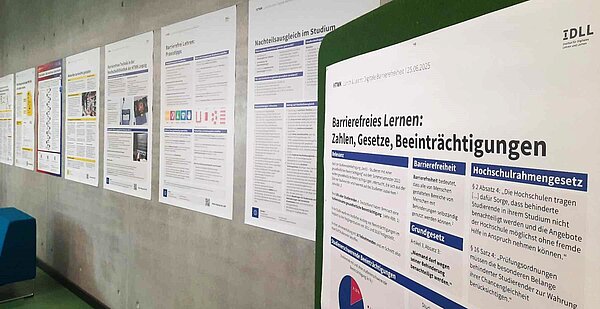 Posterausstellung an einer grauen Betonwand sind Poster in Größe A0 in einer Reihe aufgehangen, im Vordergrund ist das Poster mit dem Titel " Barrierefreies lernen: Zahlen, Gesetze, Beeinträchtigungen" zu sehen